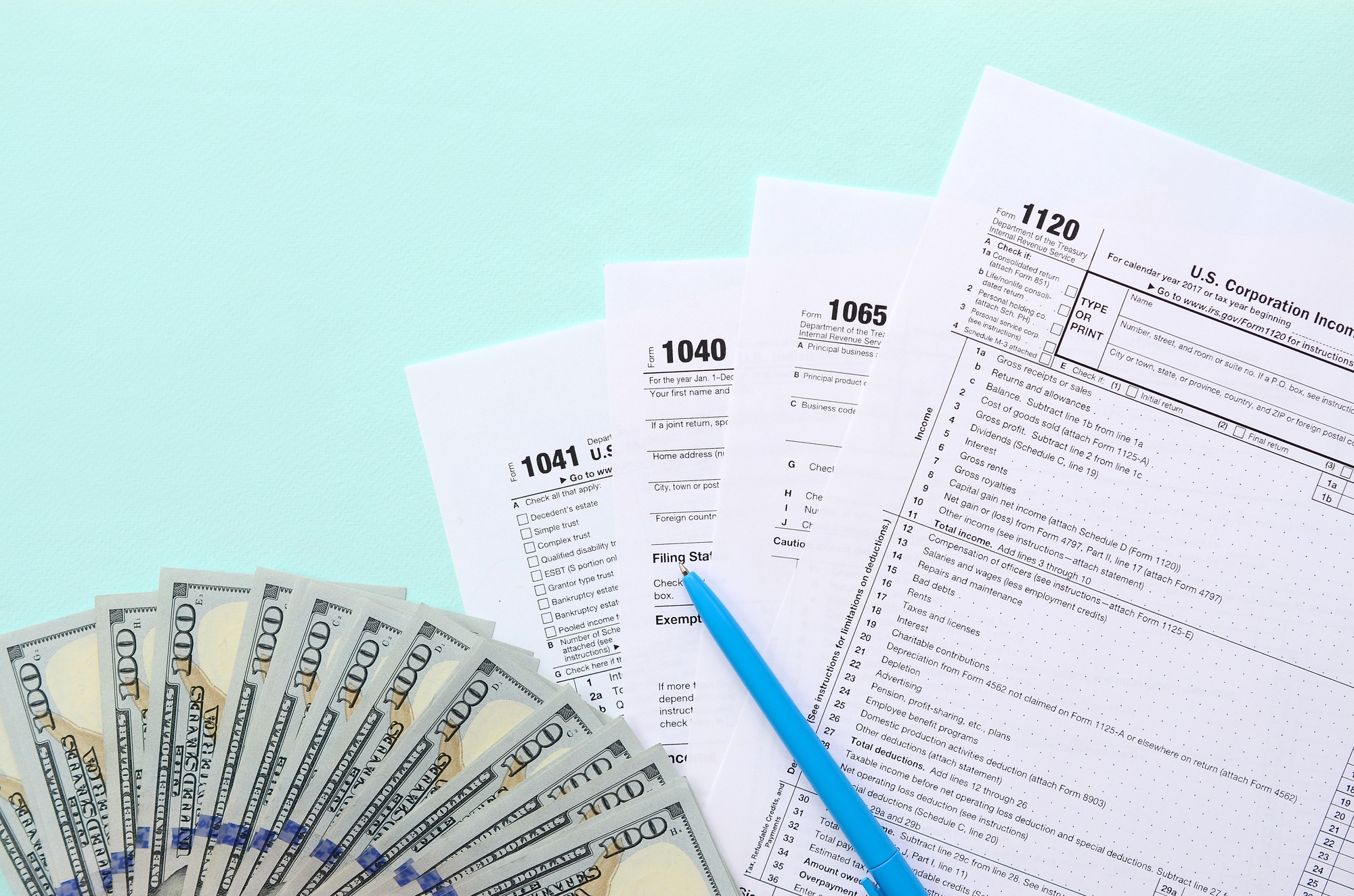 Tax forms lies near hundred dollar bills and blue pen on a light blue background. Income tax return.